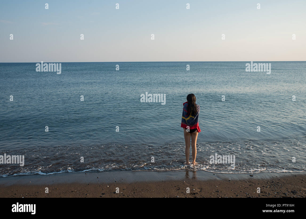 Jugendlich stehend an Water's Edge mit Handtuch mit Blick auf das Meer Stockfoto