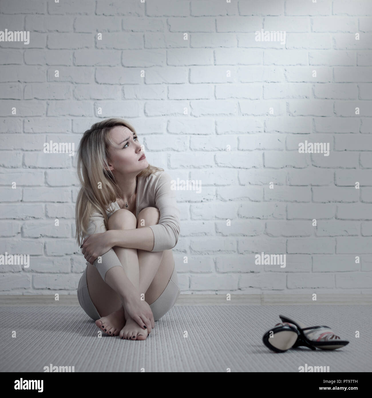 Junge traurige Frau sitzen auf dem Boden in der Nähe der Mauer. Stockfoto