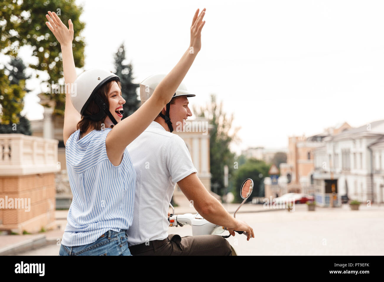 Rückansicht des glückliches junges Paar in Sturzhelme reiten auf Roller zusammen im Freien Stockfoto