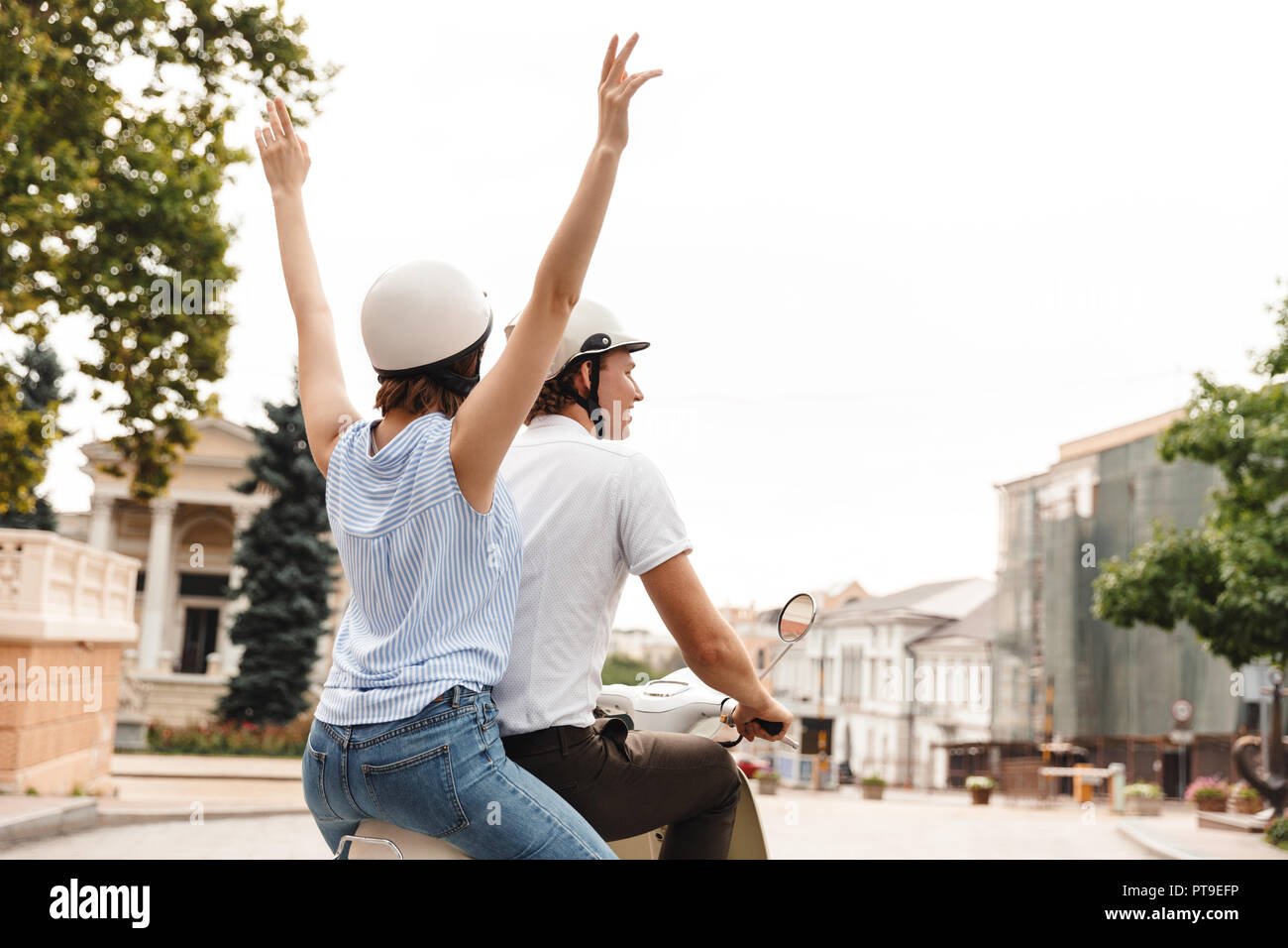 Rückansicht des fröhlichen jungen Paares im Sturzhelme reiten auf Roller zusammen im Freien Stockfoto