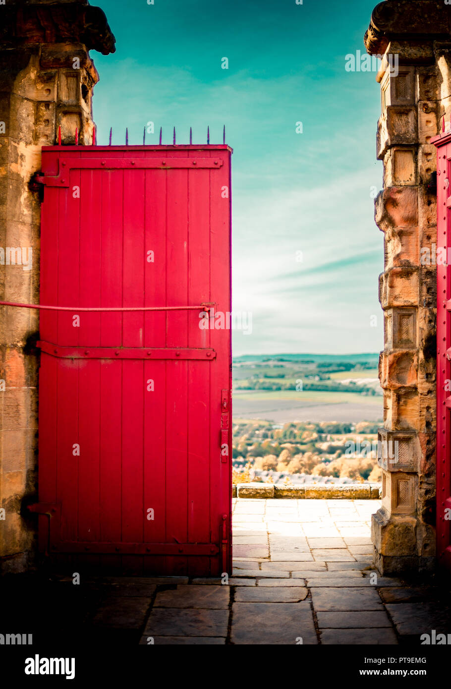 Eine große, helle rote Tür vor blauem Himmel mit Blick auf eine lange Vista an einem sonnigen Herbsttag. Stockfoto