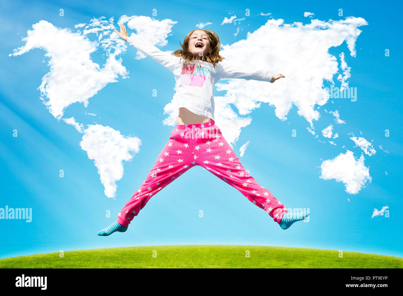 Happy girl springen hoch auf einem grünen Gras gegen die Wolken in der Form von Welt Karte während der sonnigen Tag. Stockfoto