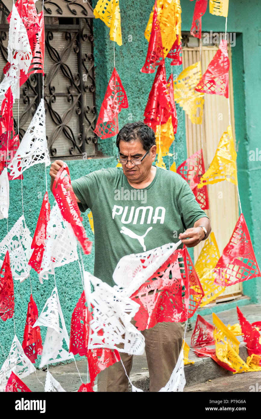 Eine mexikanische Mann arbeitet, um Papel picado Banner entwirren in der Vorbereitung für die 8. Nacht Gedenkfeier zum Ende des Festes des Hl. Michael in der mexikanischen Stadt Uriangato, Guanajuato. Jedes Jahr schmückt die Stadt 5 km Fahrt mit religiösen Symbolen in der Vorbereitung für die Statue der Schutzheiligen durch die Stadt zu vorgeführt werden. Uriangato wurde eine internationale Sensation nach wowing Brüssel mit Ihren geblümten Teppich auf dem Brüsseler Grand-Place während der Belgien geblümten Teppich Festival angezeigt. Stockfoto