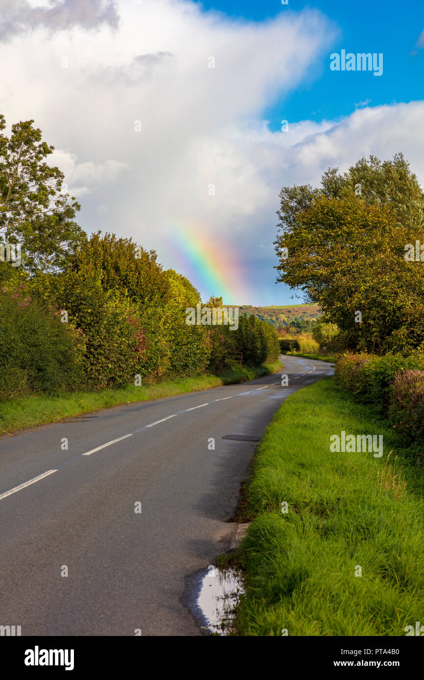 Ein Regenbogen über dem B4368Craven Arms zu Clun Straße, spiegelt die Farben in der Landschaft im Herbst Farben beginnen, da die Bäume biegen, Shropshire, Großbritannien Stockfoto