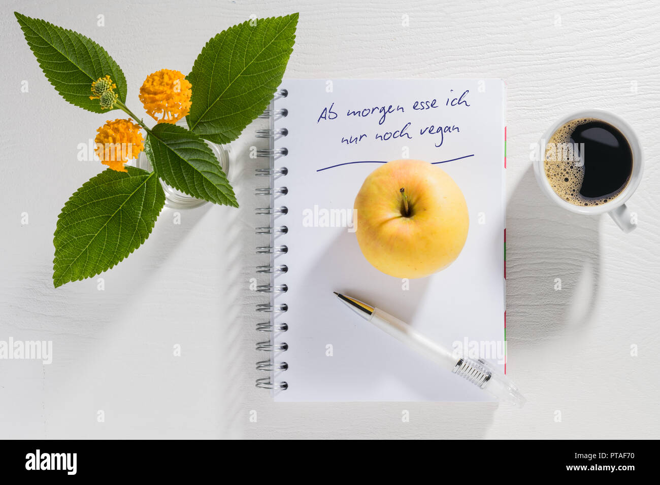 Schreibblock mit Auflösung des neuen Jahres mit Kaffeetasse und Blumen auf einem weißen Tisch Stockfoto