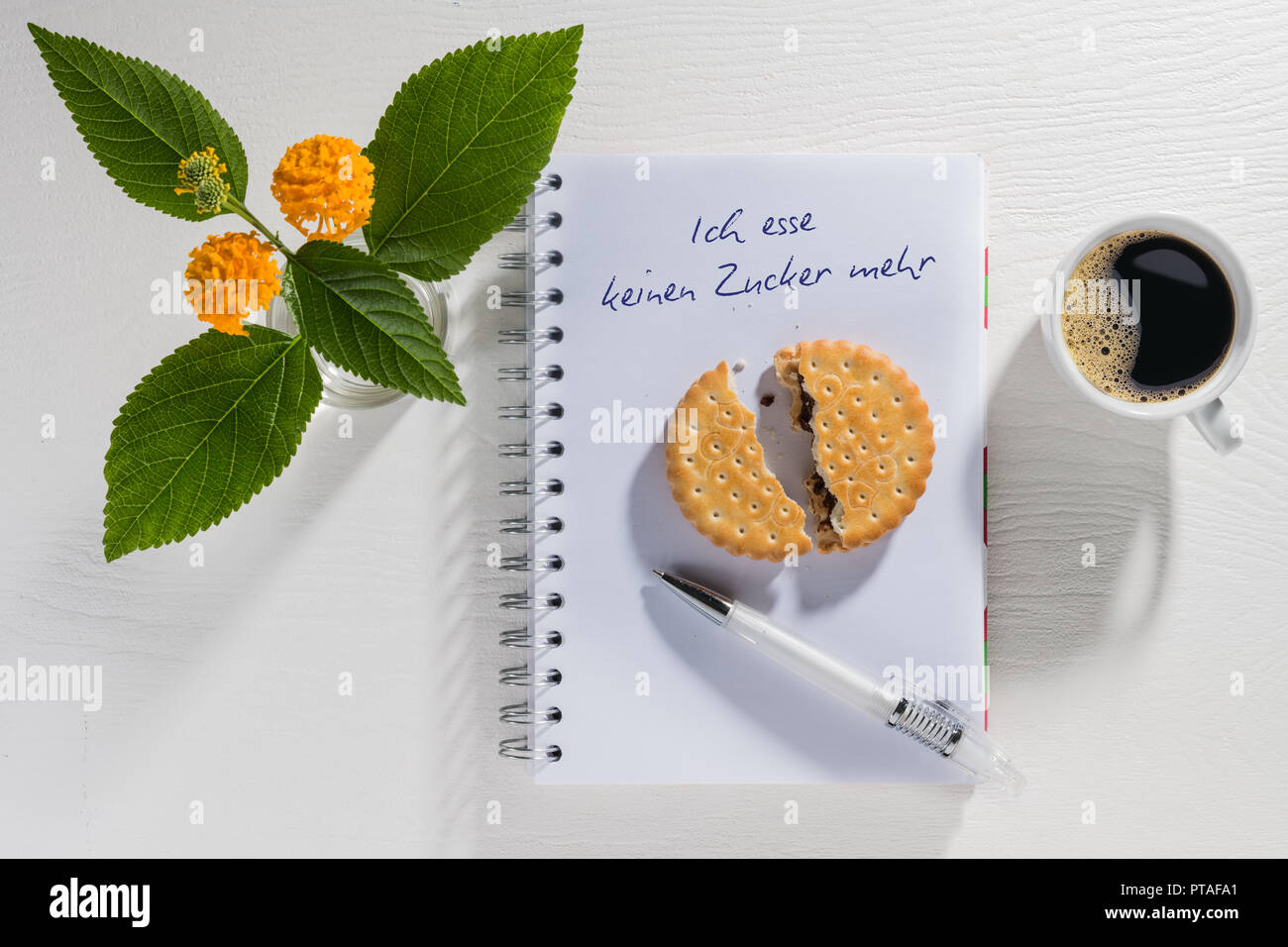 Schreibblock mit Auflösung des neuen Jahres mit Kaffeetasse und Blumen auf einem weißen Tisch Stockfoto