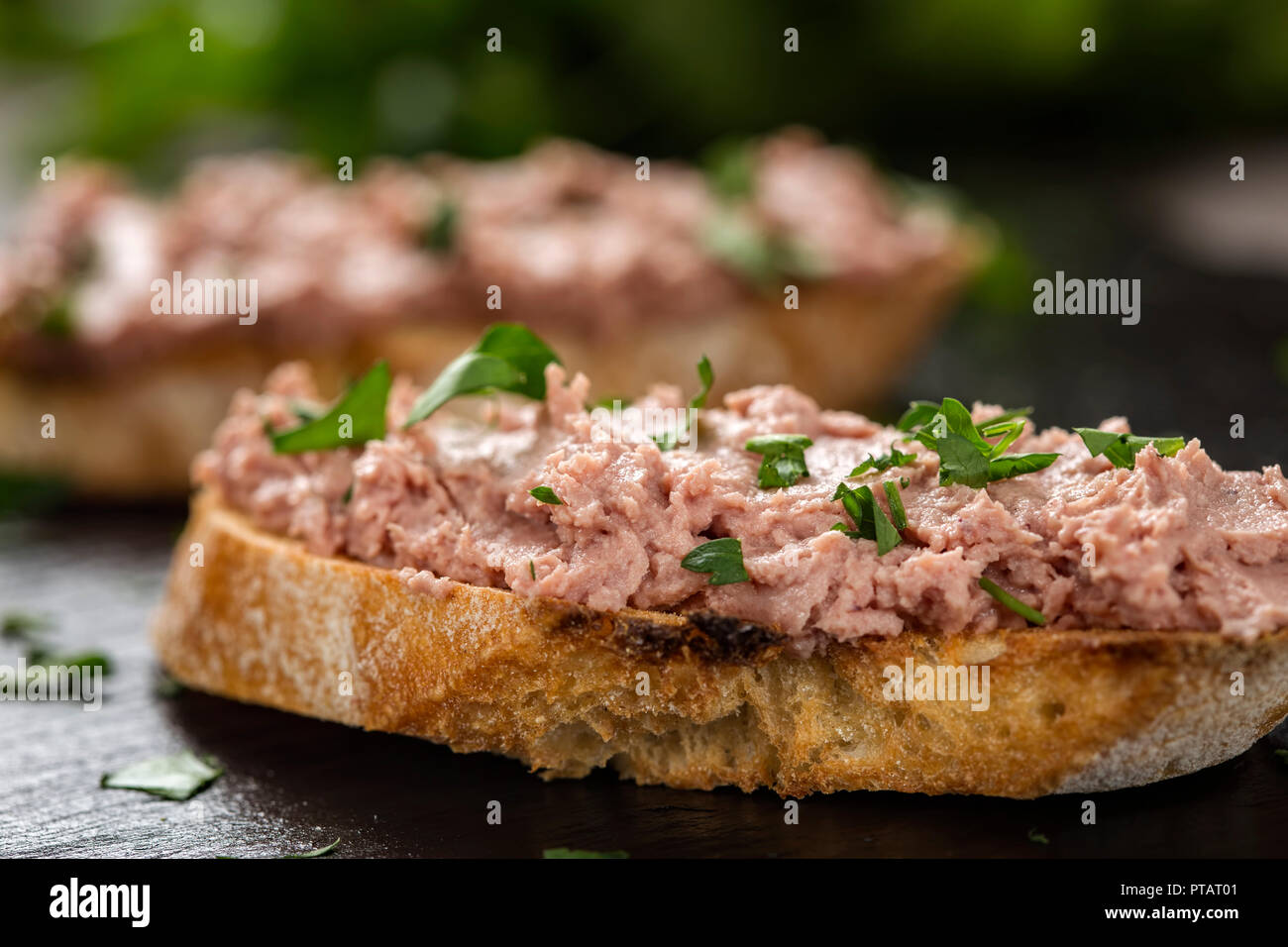 Leberwurst Sandwich mit gehackter Petersilie auf dunklem Schiefer als detaillierte Nahaufnahme (selektive Fokus) Stockfoto