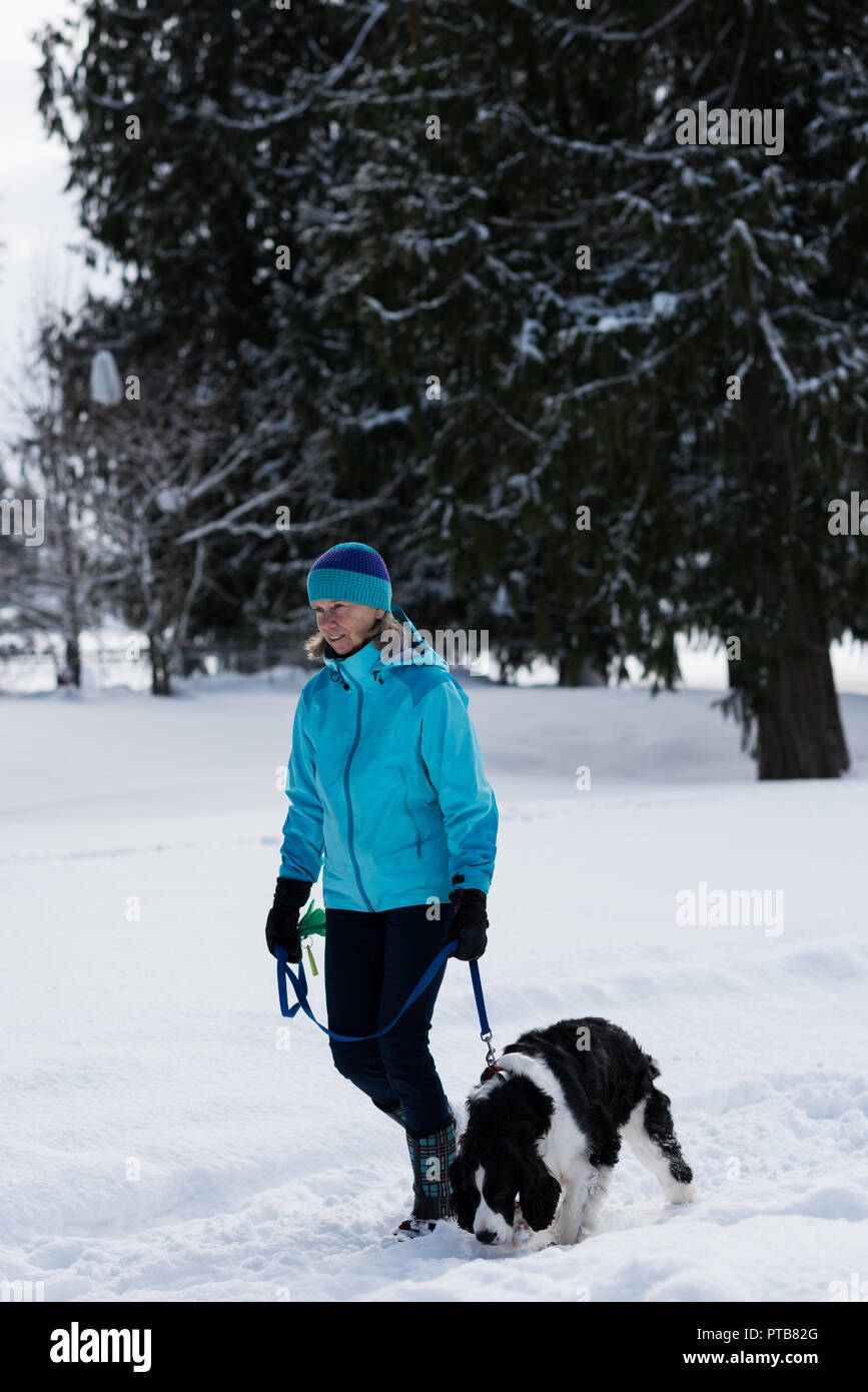 Ältere Frau gehen mit Ihrem Hund in verschneiter Landschaft Stockfoto