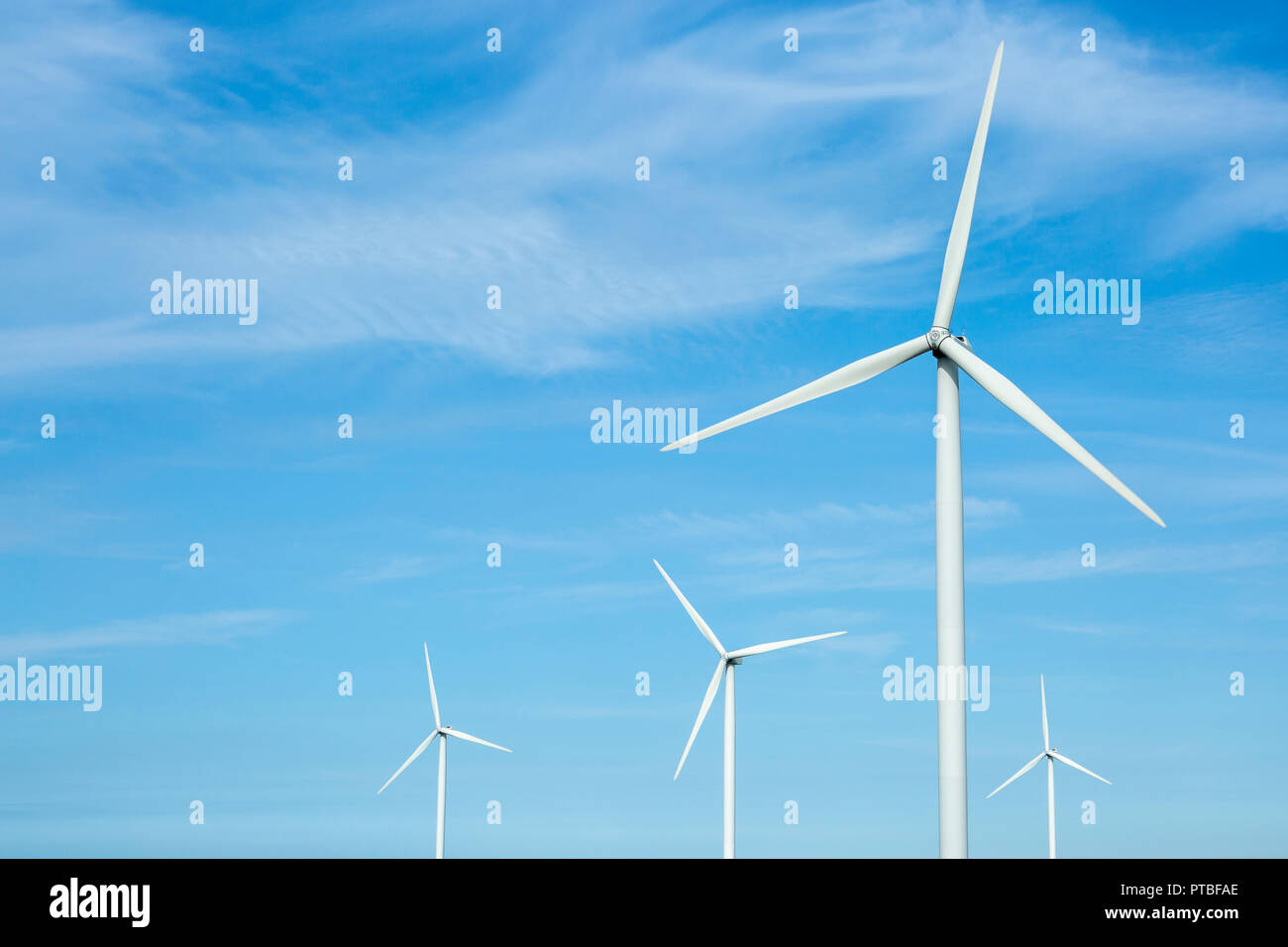 Vordere Nahaufnahme von vier beweglichen windenergieanlagen gegen sonnigen Licht blauer Himmel, Niederlande, Europa Stockfoto