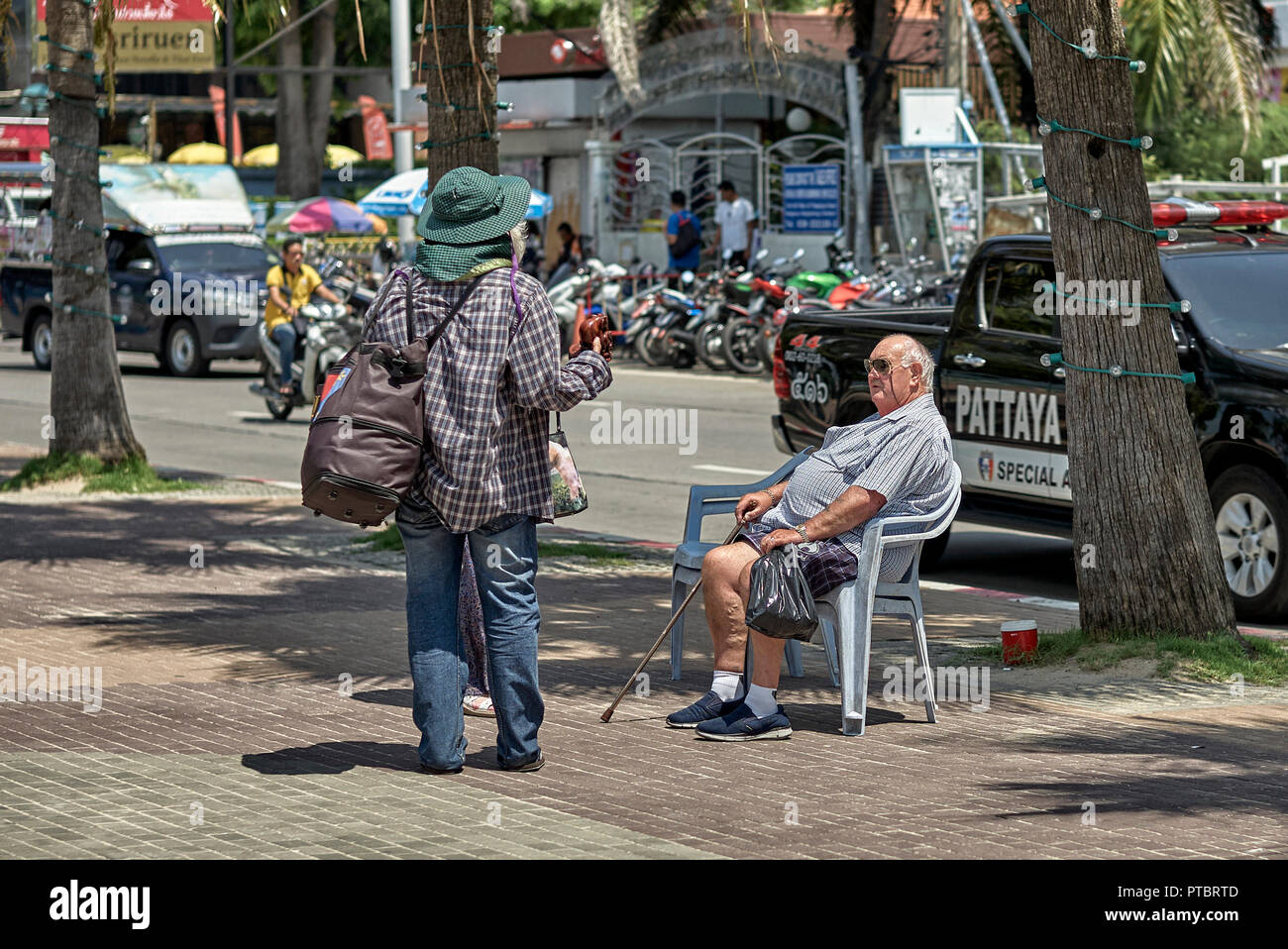 Thailand Straßenverkäufer bietet Souvenirs für einen älteren männlichen Touristen entspannen auf dem Bürgersteig. Pattaya, Thailand, Südostasien Stockfoto