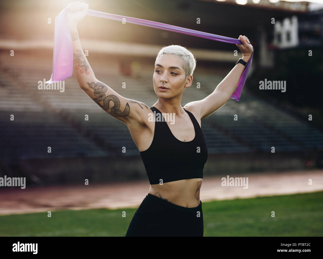 Frau Runner in einem Leichtathletik Stadion zu tun Stretching Übungen mit einem Widerstand Band. Athletische Frau in Fitness Kleidung, warme Stockfoto