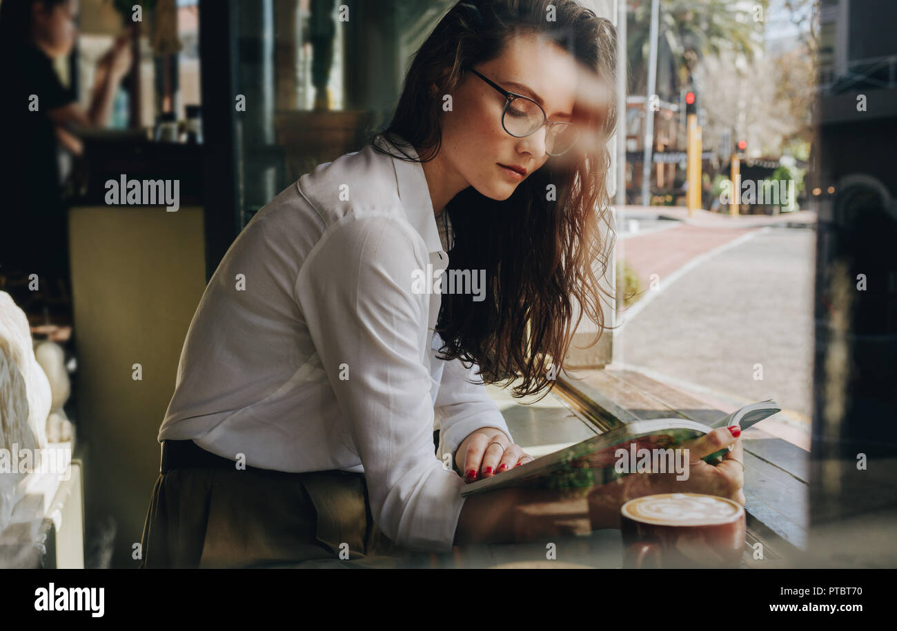 Junge Frau am Fenster Cafe sitzen und lesen ein Buch. Kaukasische Frauen mit Brille Buch im Coffee Shop. Stockfoto