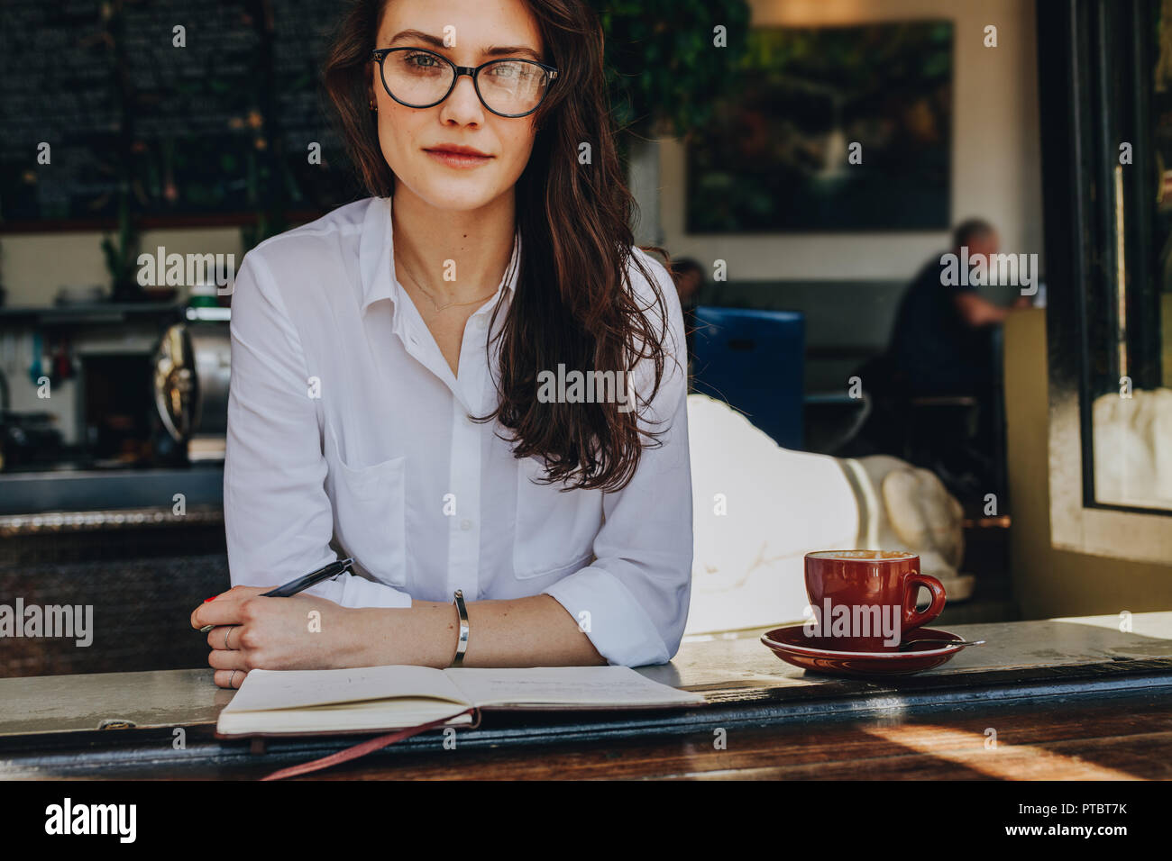 Portrait von selbstbewussten jungen Frau im Cafe mit Buch und Tasse Kaffee am Tisch sitzen. Kaukasische Frau entspannen im Cafe. Stockfoto