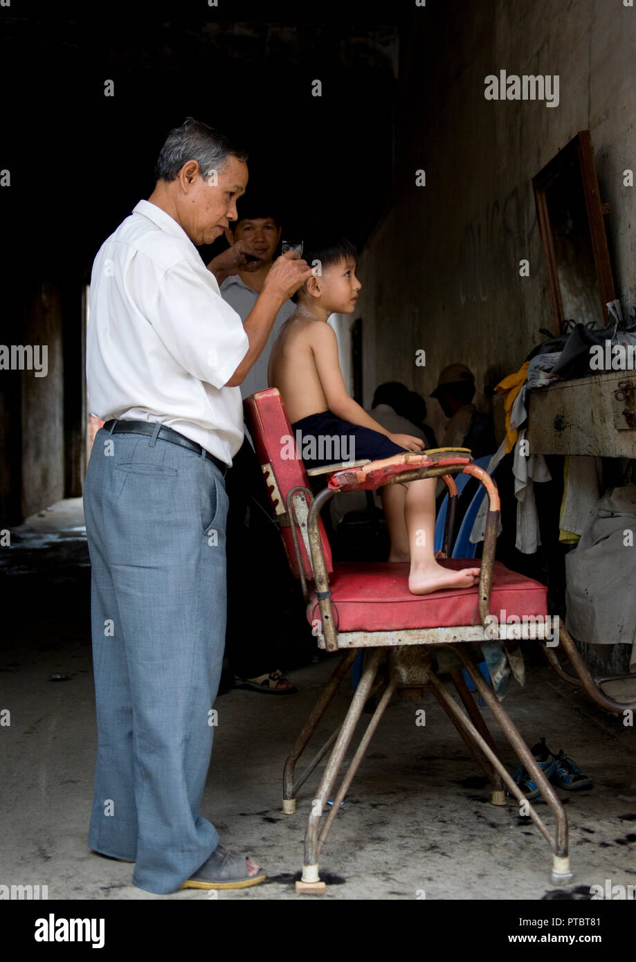 Ein Junge, der sich die Haare von einem Mann in einem Salon, Phnom Penh Provinz, Phnom Penh, Kambodscha schneiden Stockfoto