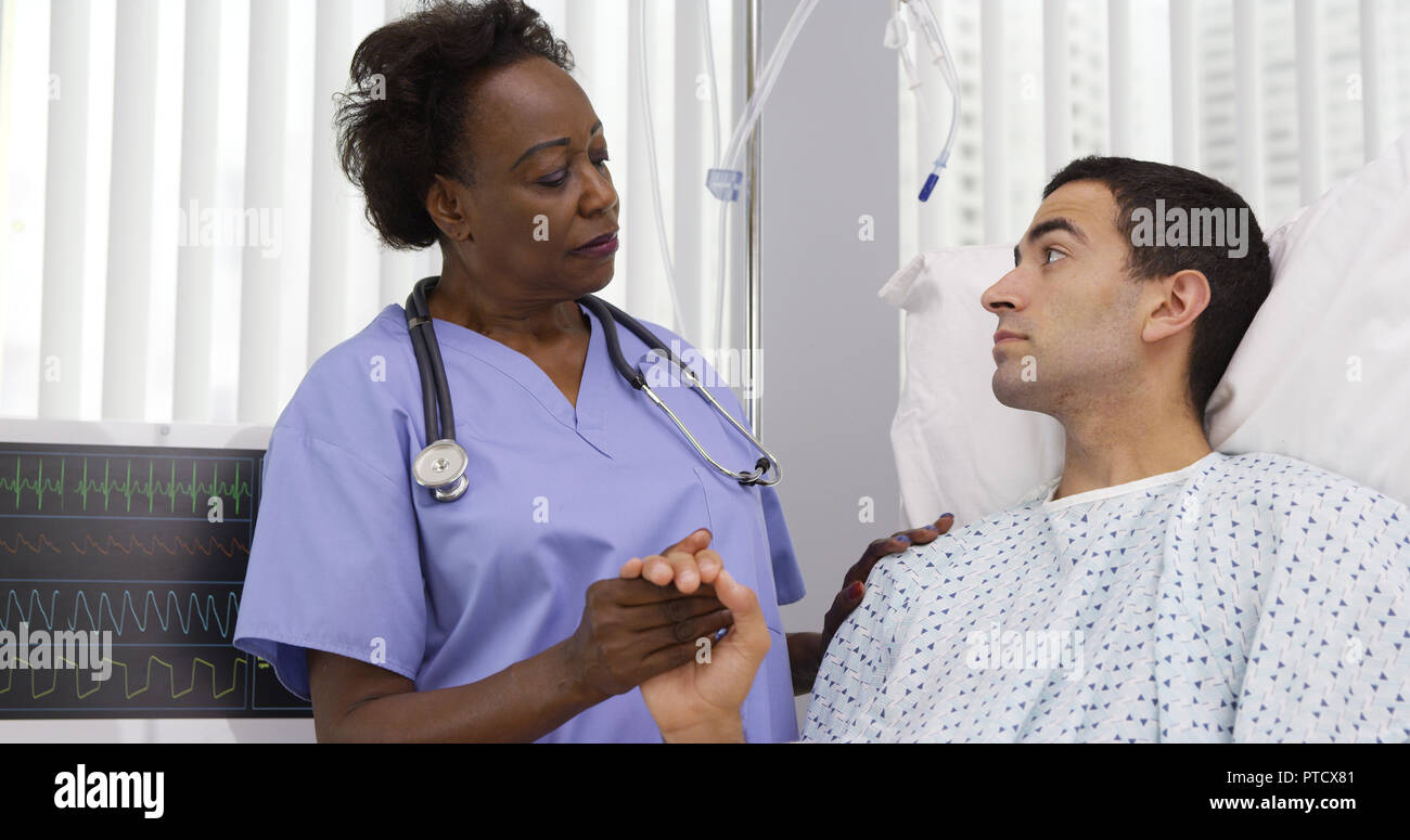 Senior schwarz Krankenschwester tröstlich junge Hispanic Patienten am Krankenbett Stockfoto