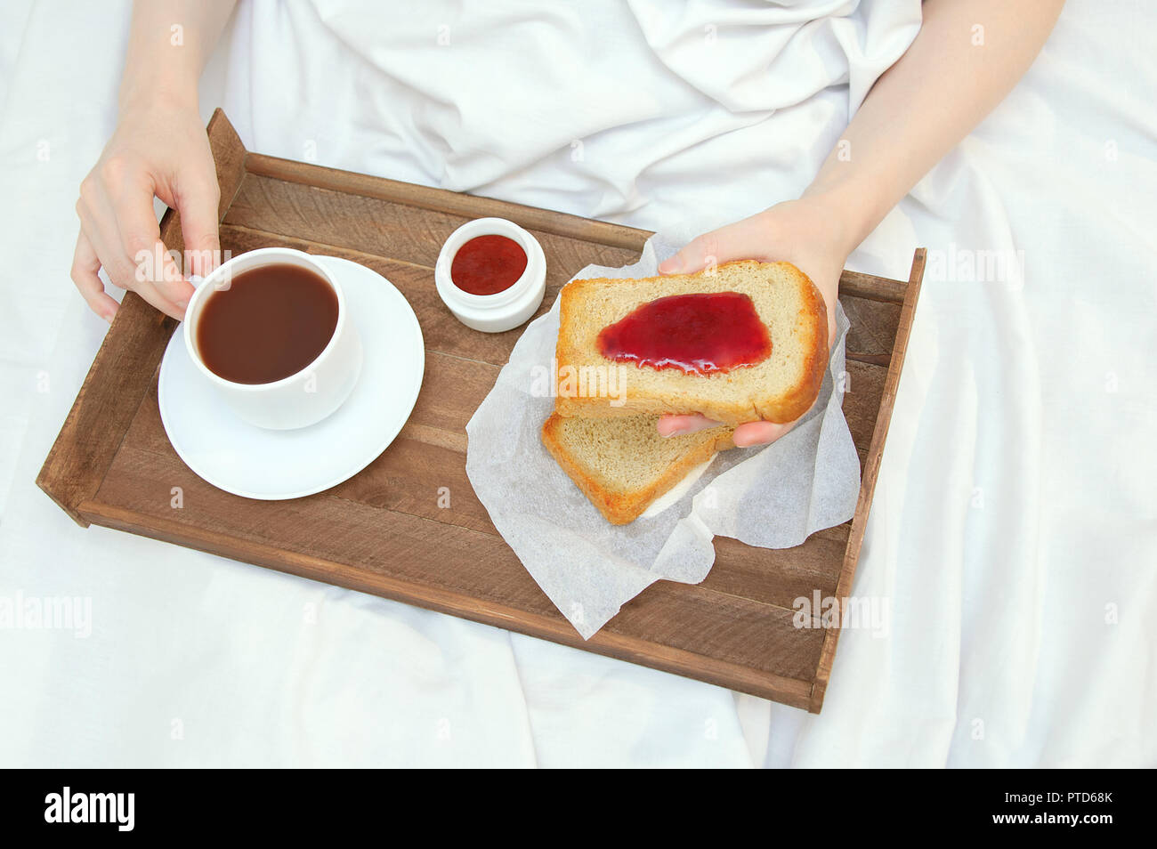 Das Mädchen ist Frühstück im Bett, mit Holz- Fach mit Toast mit Marmelade und Kakao Stockfoto
