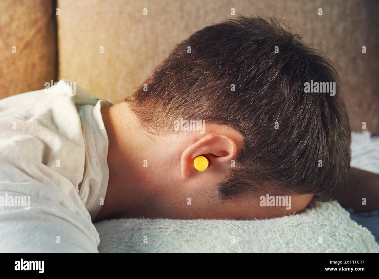 Schöne junge Mann schlafen, in die Ohren gelben Ohrenstöpsel gegen Straßenlärm, Rettung von der lauten Nachbarn. wenn Schlaf verhindern. Stockfoto