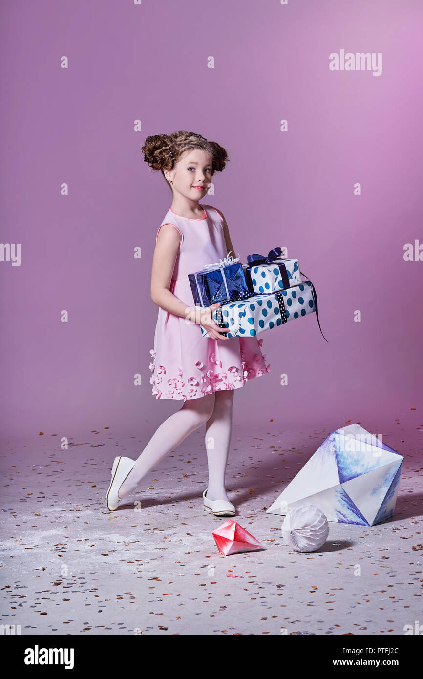 Dame kleines Mädchen in schönen rosa Kleid mit Geschenk vorhanden. Mode Kind. Feiertage, Weihnachten, Neues Jahr, X-mas-Konzept. In voller Länge Porträt lächelndes Kind in Studio posiert, rosa Hintergrund. Stockfoto