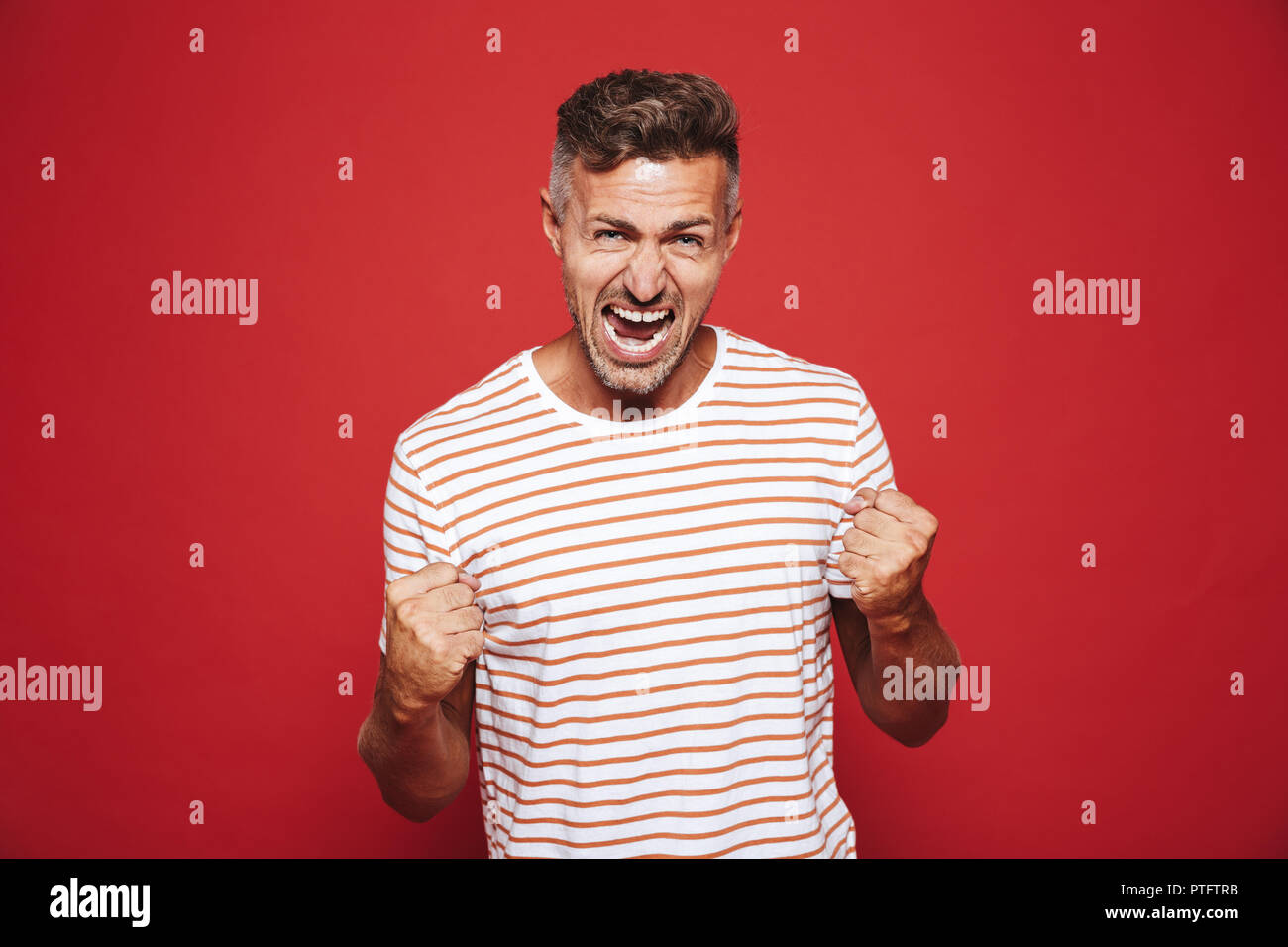 Emotionale wütenden Mann in gestreiften T-Shirt zu schreien und die fäuste über den roten Hintergrund isoliert Stockfoto