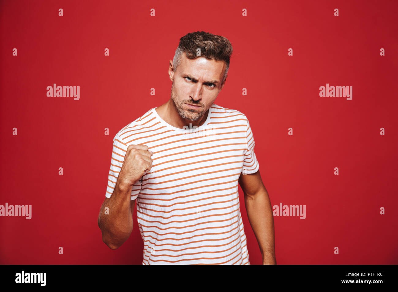 Aggressive Mann in gestreiften T-Shirt mit Abscheu und zeigt Faust über den roten Hintergrund isoliert Stockfoto