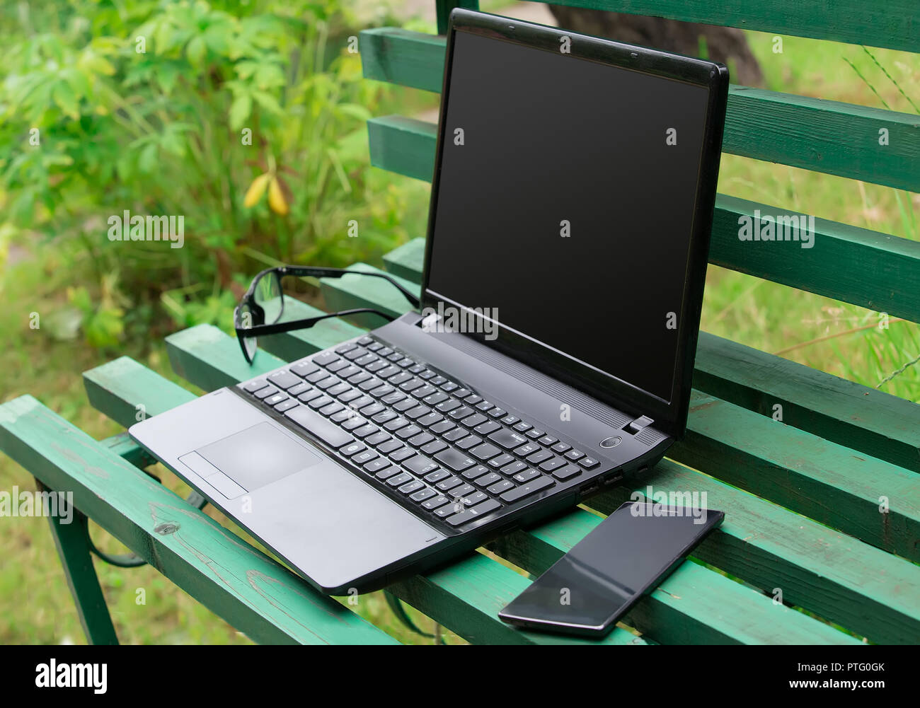 Laptop, Smartphone und Gläser auf einer Parkbank Stockfoto
