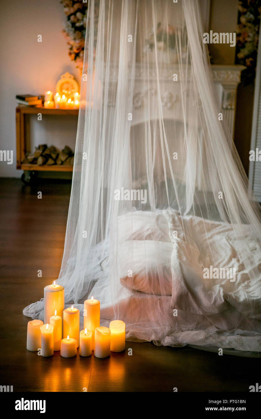 Loft-stil Zimmer mit einem Bett, einem Baldachin, ein weißer Kamin mit einem Blumenarrangement, Kerzen, close-up Stockfoto
