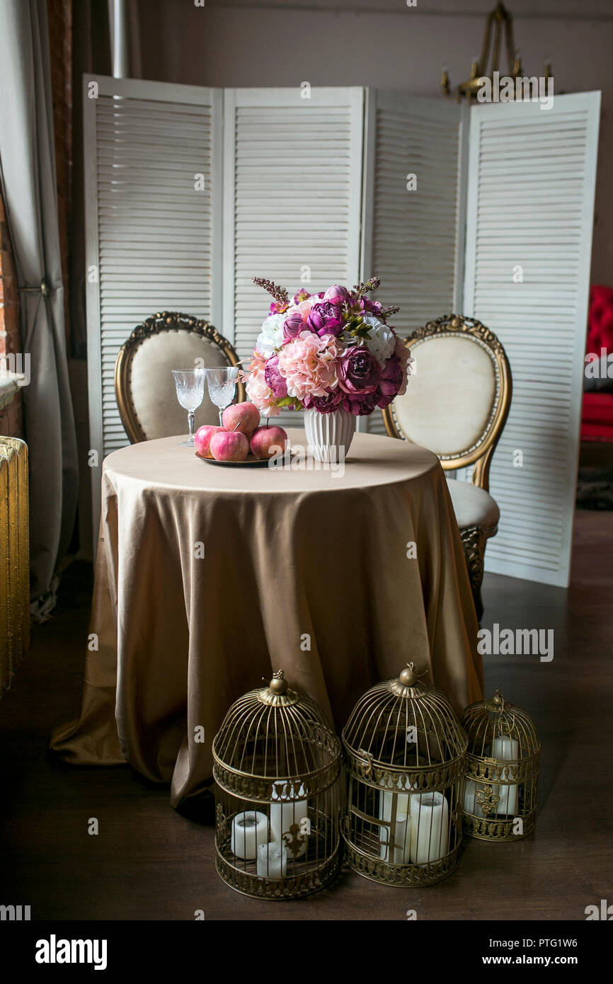 Esstisch mit Stühlen, einem Bildschirm, Früchte, eine Vase mit Blumen, Kerzen in den Dachboden, Vorderansicht Stockfoto