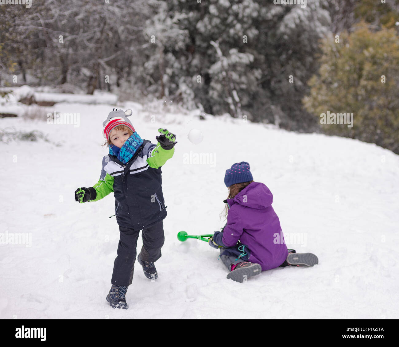 Junge Junge wirft einen Schneeball, während ein junges Mädchen mehr Schneebälle macht Stockfoto