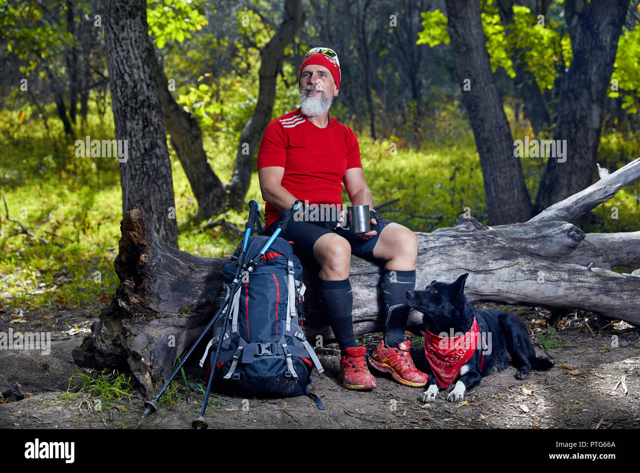 Bärtiger Mann im roten T-Shirt mit Hund im Wald. Outdoor Travel Concept Stockfoto