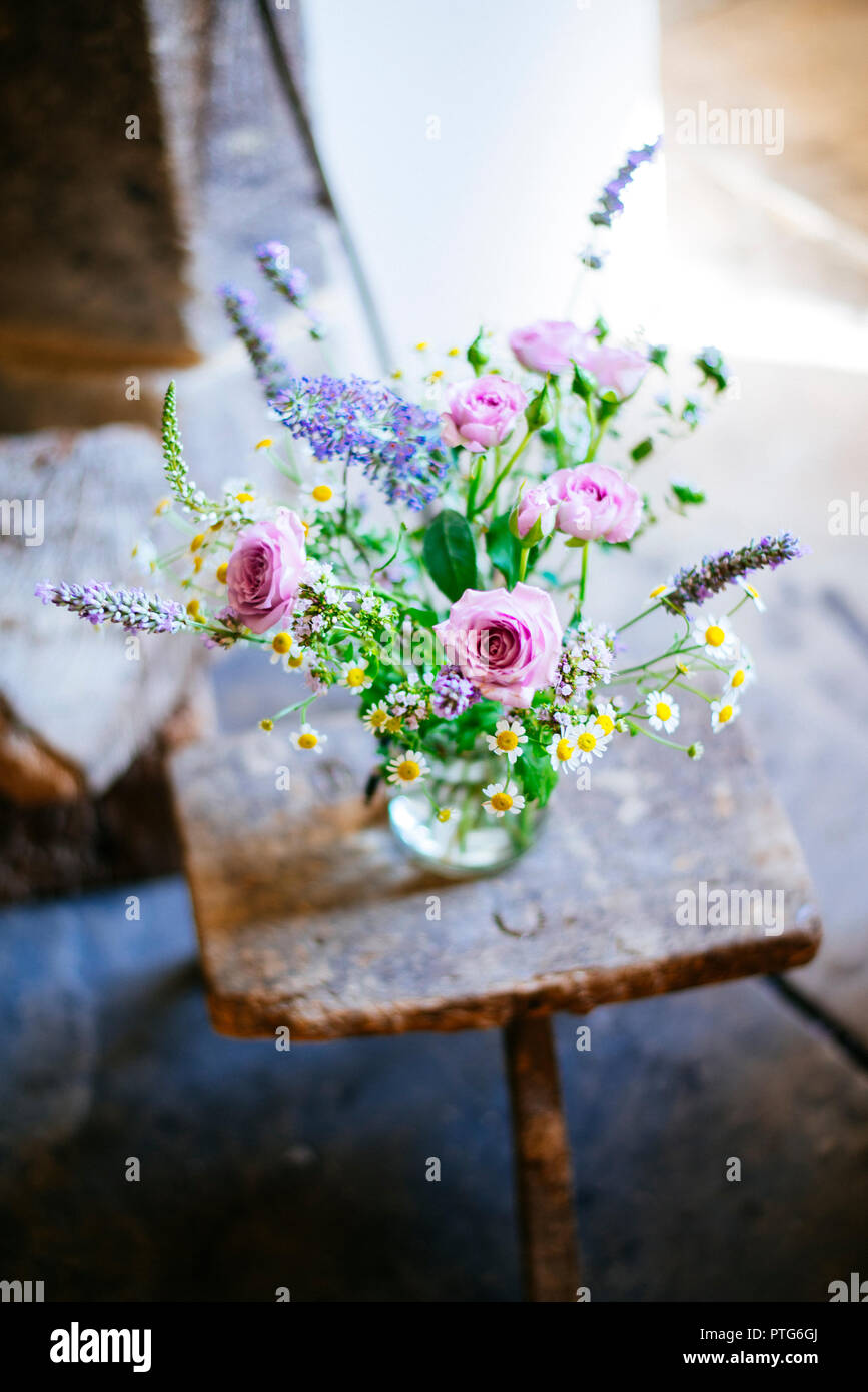 Glas mit Blumen auf einem rustikalen Hocker Stockfoto