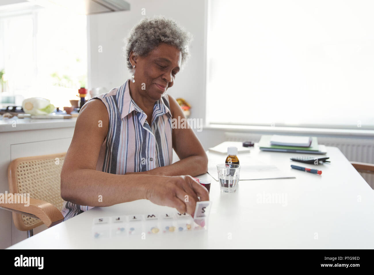 Ältere Frau Organisation Pille Box am Küchentisch Stockfoto