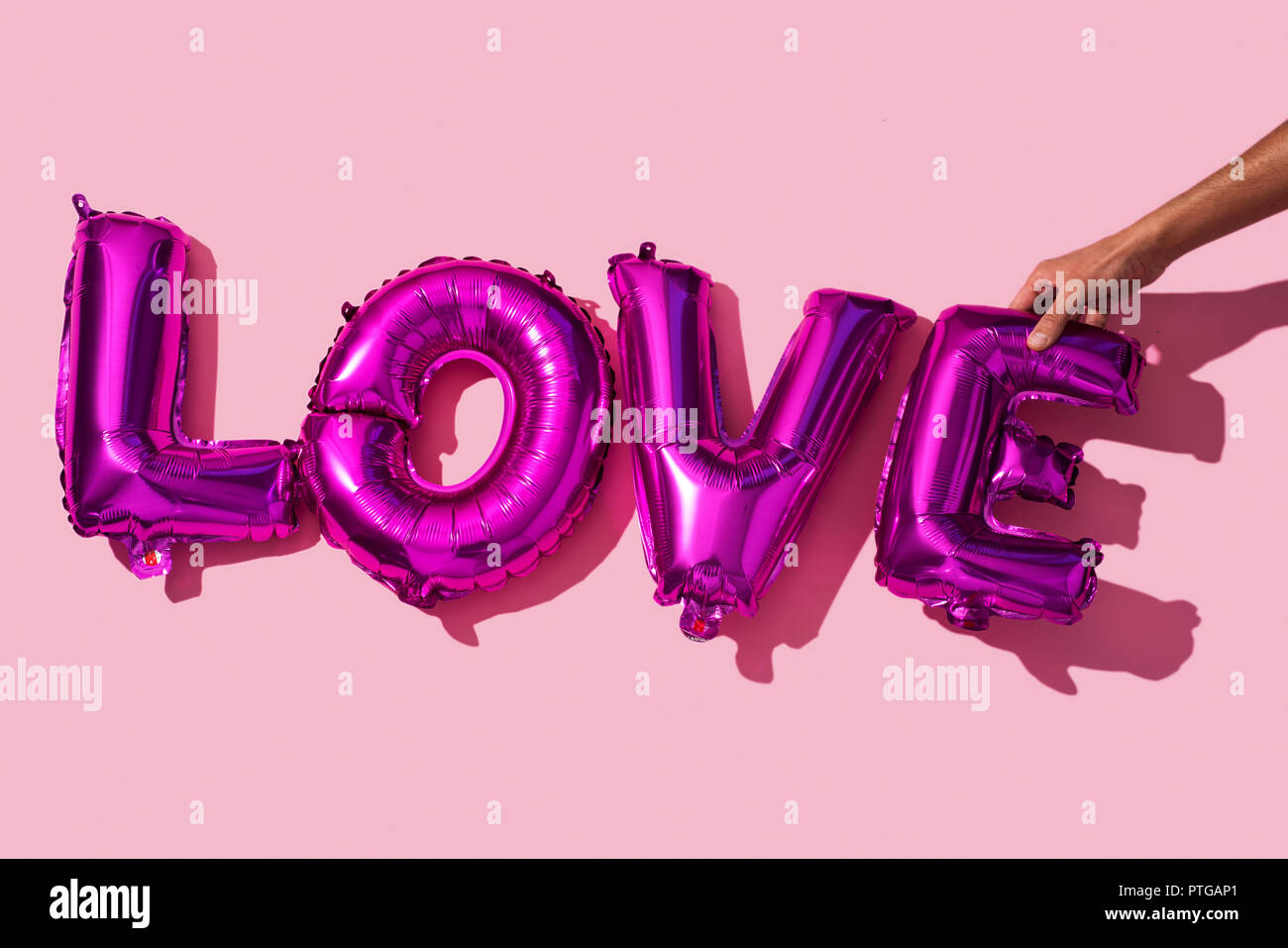 Junge Menschen, die das Wort Liebe mit einigen fuchsia Brief-förmige Luftballons auf einem rosa Hintergrund Stockfoto