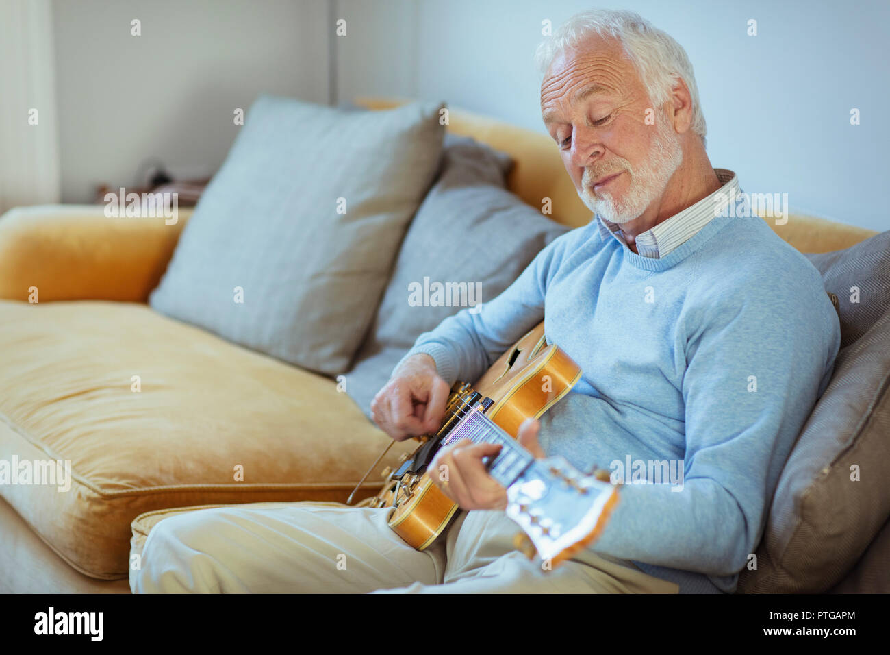 Active Senior Mann spielt Gitarre auf Sofa im Wohnzimmer Stockfoto