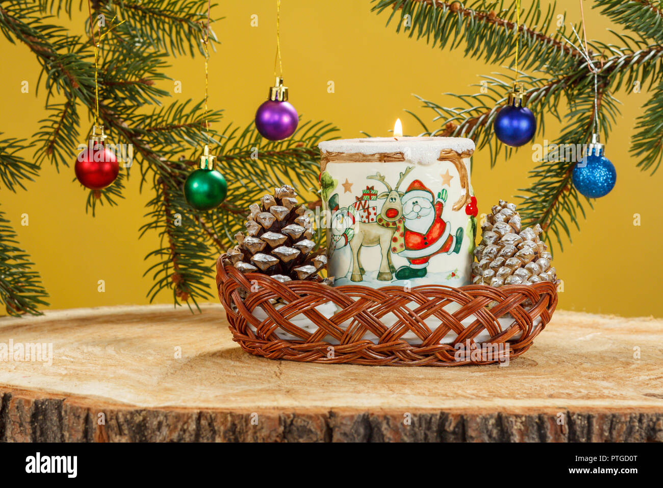 Brennende Kerze, Kegel in Weidenkorb und natürlichen Zweige Tannenbaum mit Kugeln auf Holz- Oberfläche von Pine stumpf. Weihnachten und Neujahr Konzept Stockfoto