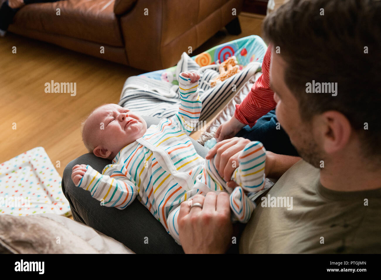 Mitte - Erwachsene Vater spielen und seine New Born Baby jungen Beine halten und ihn zu trösten versucht, während er weint. Stockfoto