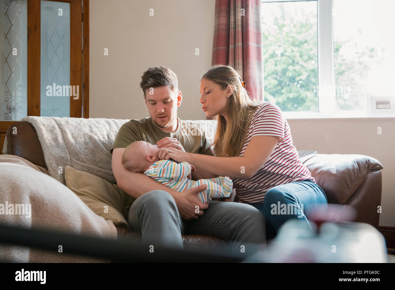 Der Mann und die Frau sitzt auf einem Sofa im Wohnzimmer mit Ihrem neugeborenen Baby. Der Mann hält das Baby und seine Frau versucht, das Baby zu erhalten Stockfoto