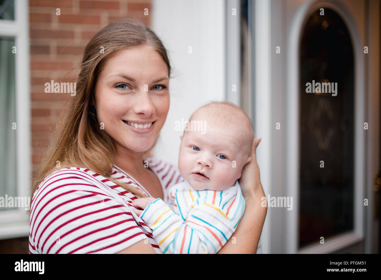 Nahaufnahme einer Mitte - Erwachsene Mutter stadning vor ihrem Haus mit Ihrem neugeborenen Baby. Sie sind sowohl mit Blick auf die Kamera und lächelnd. Stockfoto