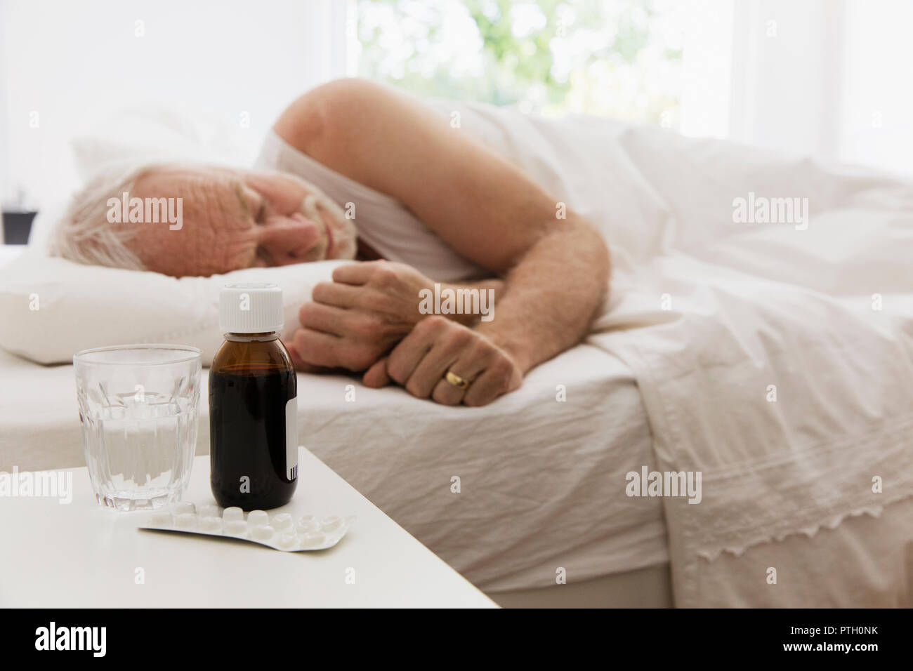 Müde älterer Mann schlafen Neben night stand mit Hustensaft und Medizin Stockfoto