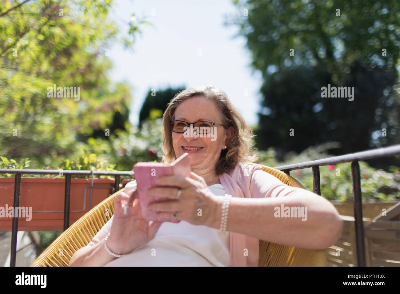 Gerne ältere Frau mit Smart Phone auf der sonnigen Terrasse Stockfoto