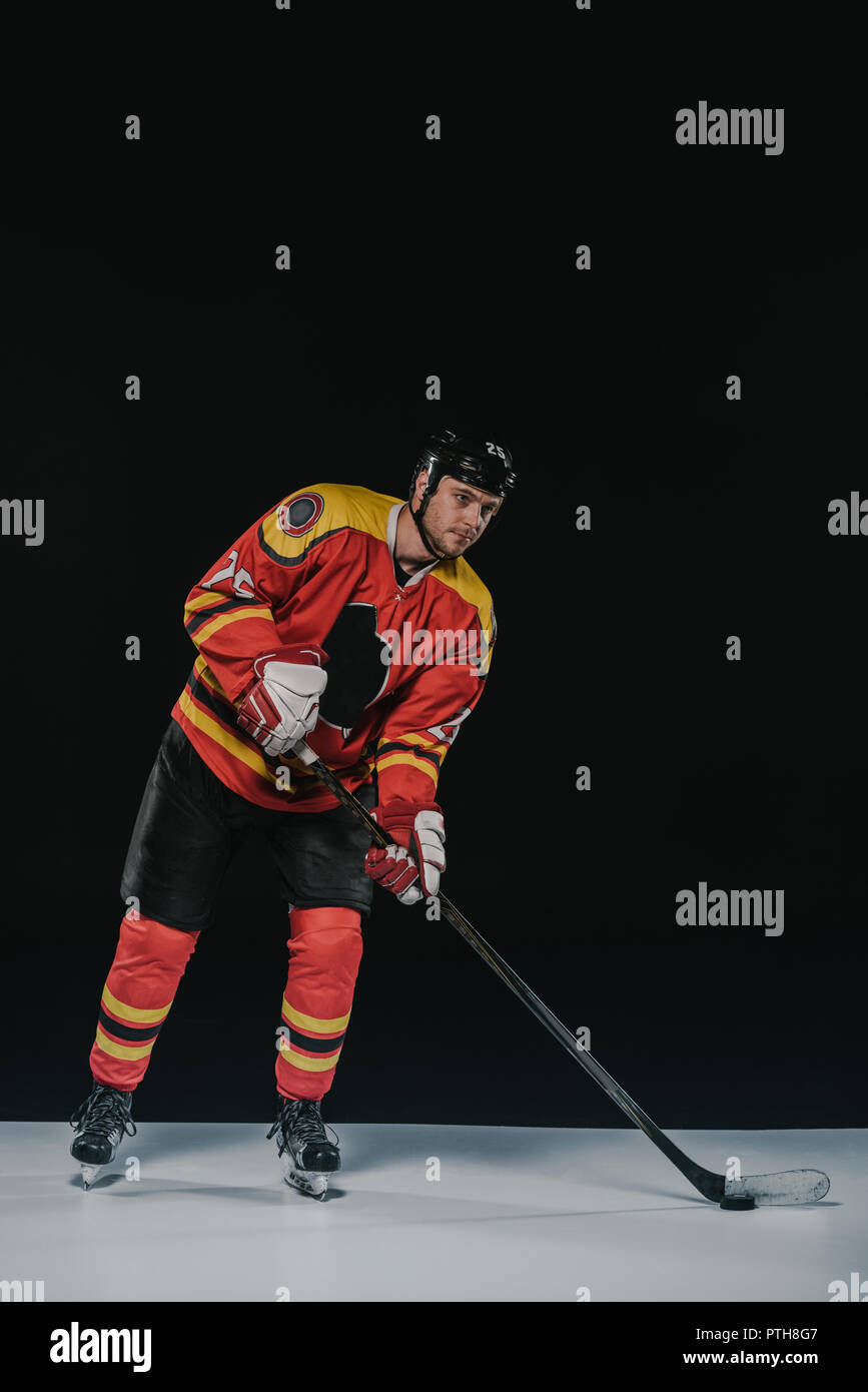 Die volle Länge der hübscher junger Sportler in sportschutzausrüstungen Hockey auf Schwarz Stockfoto