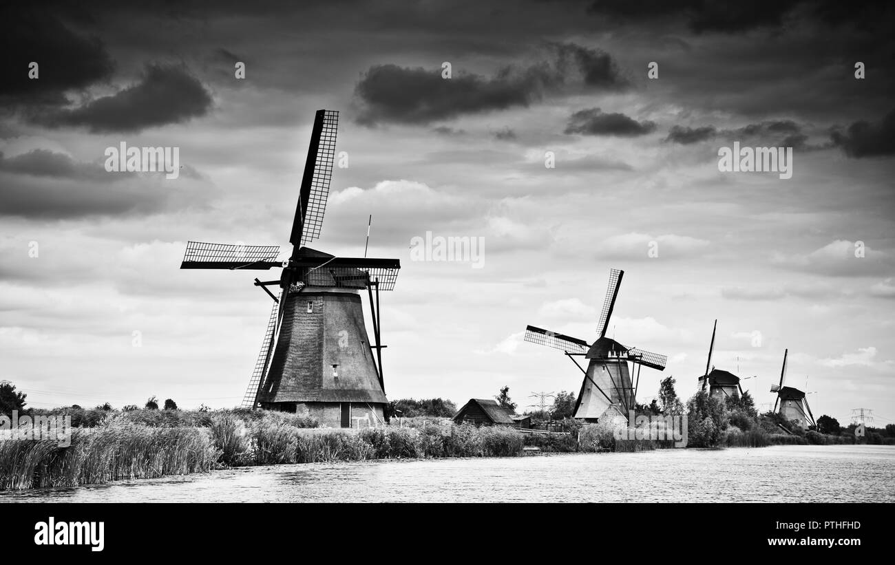Traditionelle holländische Windmühlen am Ufer des Kanals Reihen sich in den Horizont hinein, gegen einen dunklen, abgestuften Wolkenhimmel, Kinderijk, Holland, Stockfoto