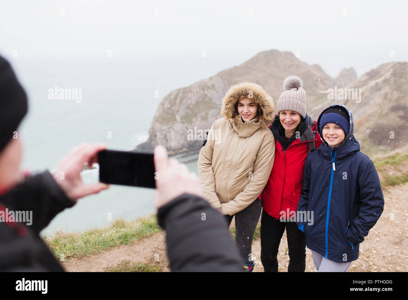 Mann mit Kamera Handy fotografieren Familie in warme Kleidung auf einer Klippe mit Blick auf den Ozean Stockfoto