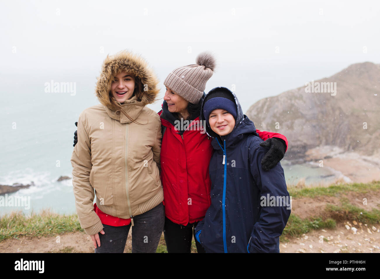 Portrait happy family in warme Kleidung steht auf einer Klippe mit Blick auf den Ozean Stockfoto