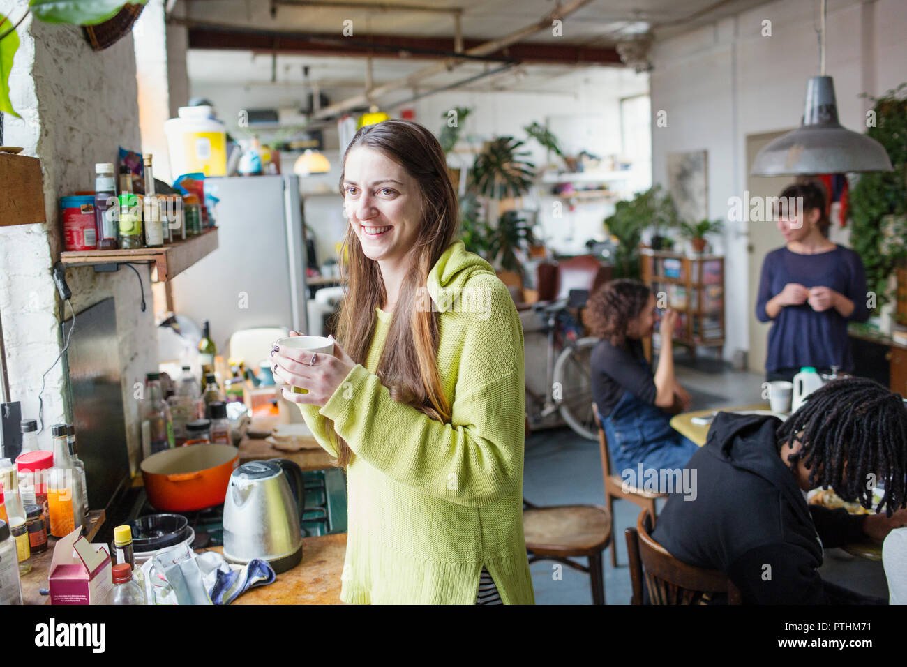 Lächelnde junge Frau trinkt Kaffee mit Mitbewohner in der Wohnung Küche Stockfoto