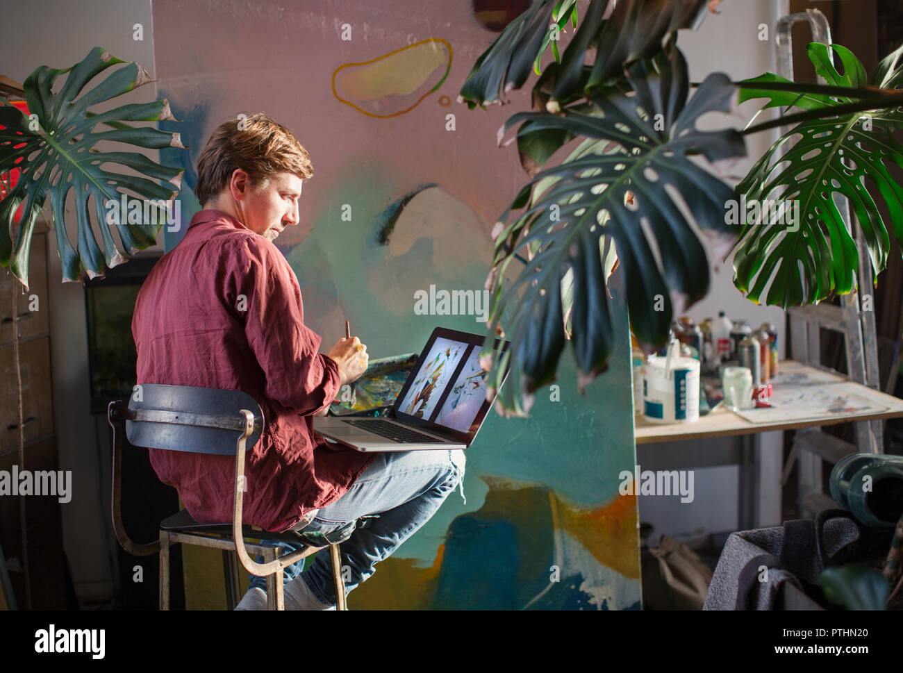 Männliche Künstler Malerei und mit Laptop in art studio Stockfoto