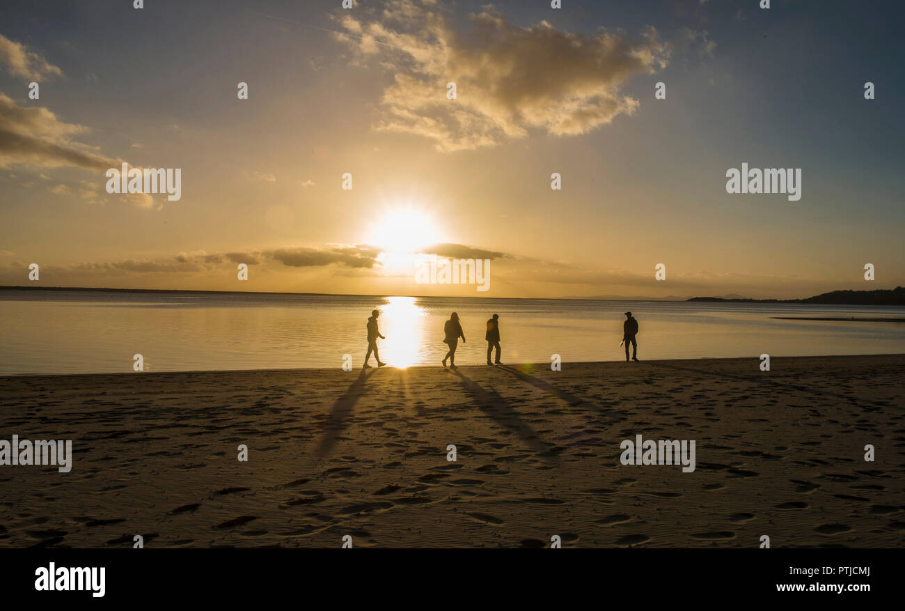 Vier Personen in silhouette Spaziergang am Strand bei Sonnenuntergang. Stockfoto