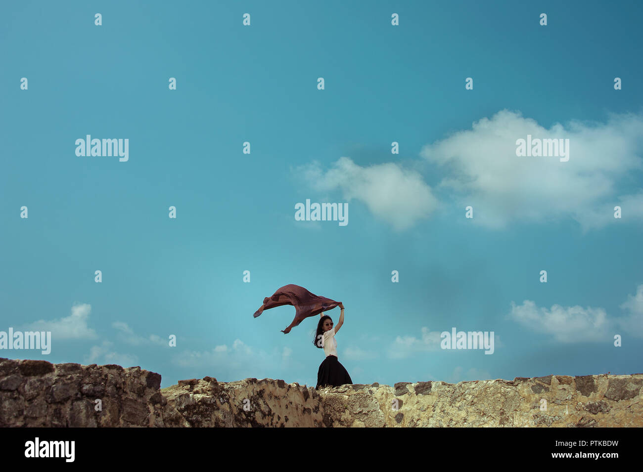 Mädchen mit Schal im Wind. Frau mit langen dunklen Haaren, Posen auf Wand gegen den blauen Himmel Hintergrund Stockfoto