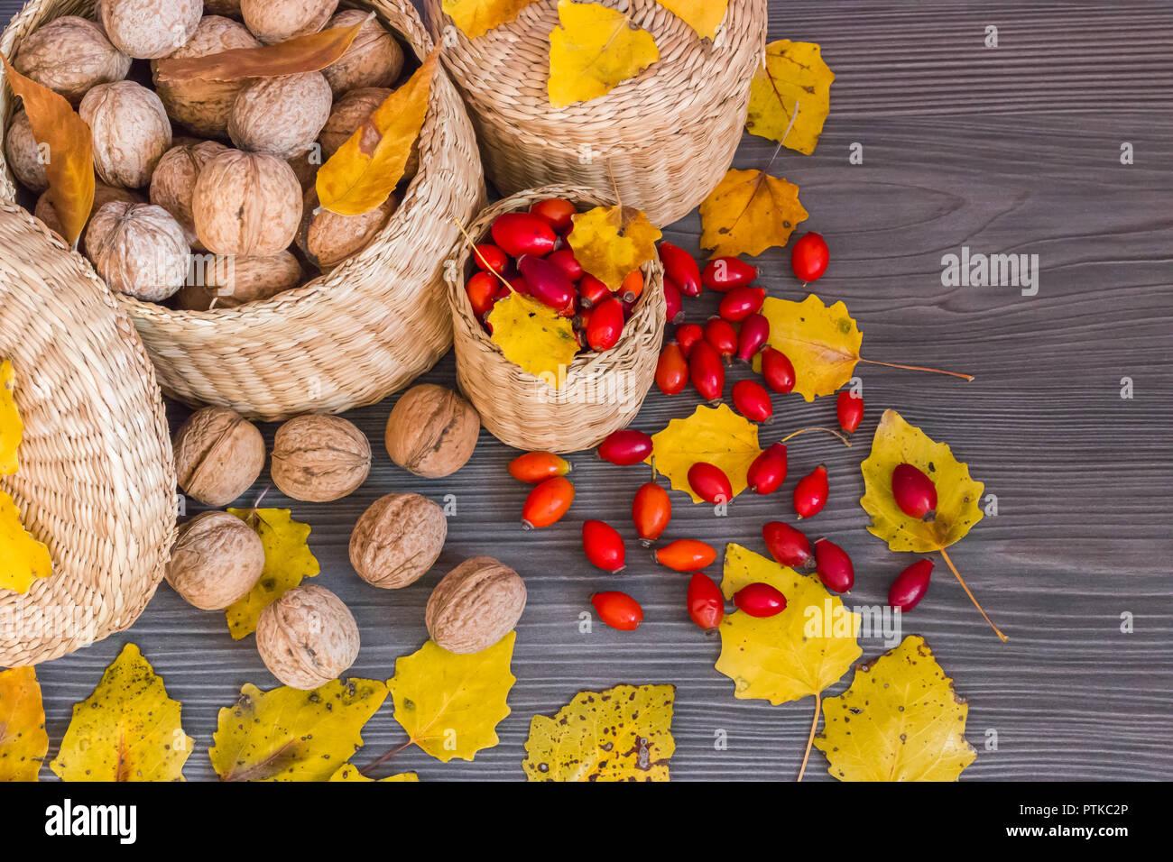 Walnüsse, Hagebutten und gelbe Blätter auf einer hölzernen Oberfläche, gesunde Nahrung aus der Natur, Konzept der Herbst Hintergrund Stockfoto
