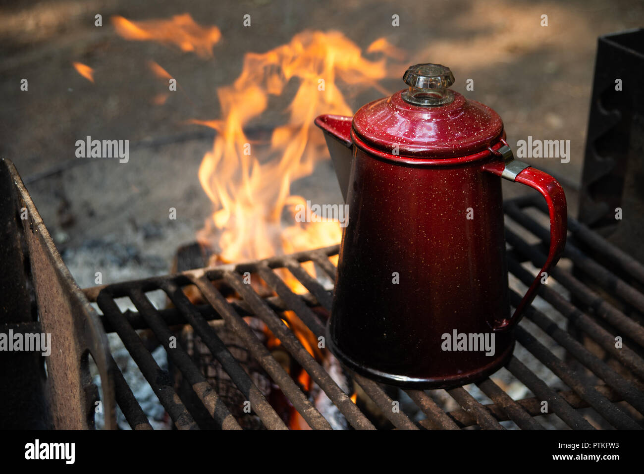 Genießen Sie eine Tasse Kaffee über einem Lagerfeuer am frühen Morgen bei Sonnenaufgang, während am Lake Crescent in Washington Camping. Stockfoto