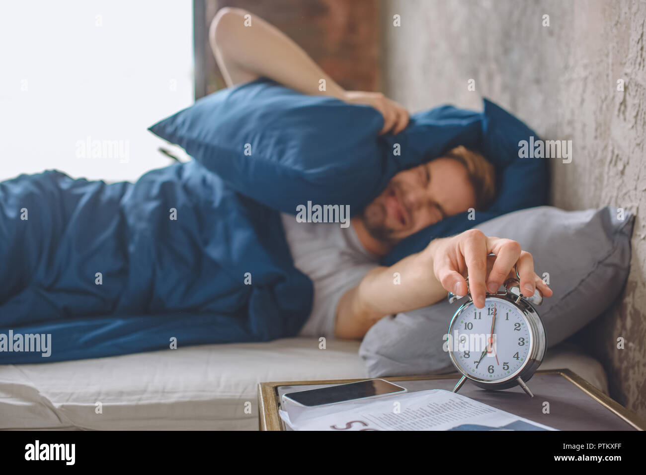 Zornigen jungen Mann im Bett schließen Ohr von Kissen und Ausschalten Wecker während der Morgen Zeit zu Hause Stockfoto
